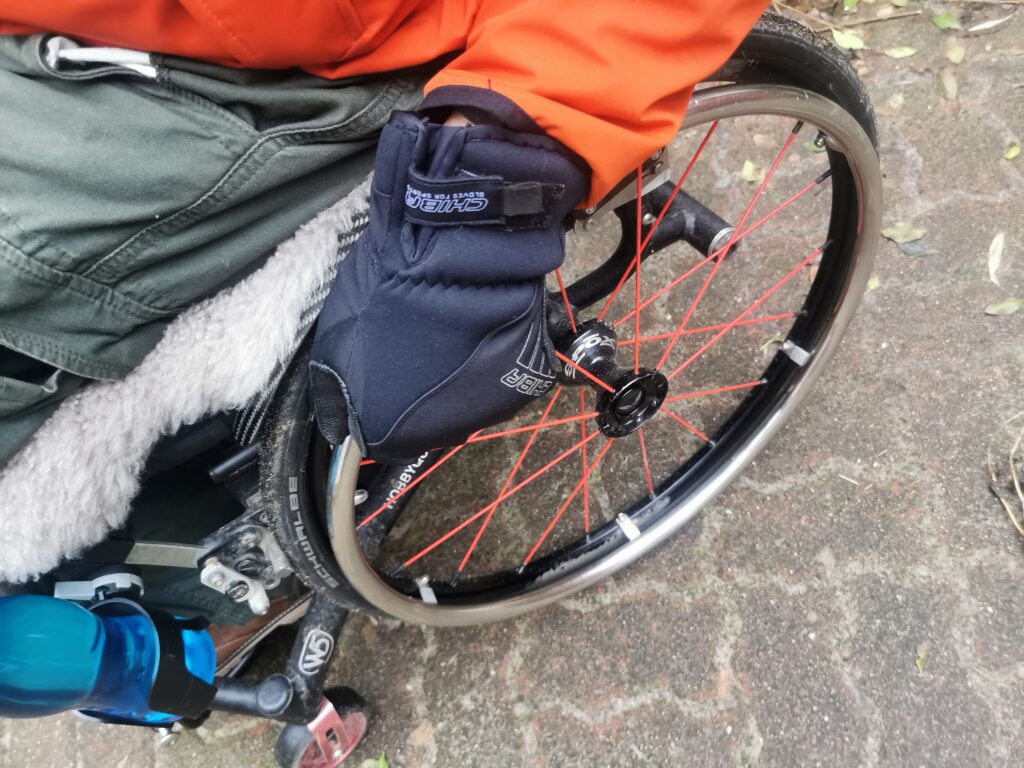 Rollstuhrad an der eine Hand mit Handschuhen den Greifreifen greift.